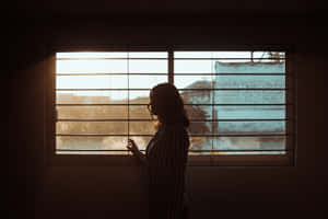 女人剪影在黃金時刻透過百葉窗凝視窗外。