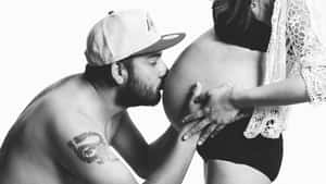 男子在黑白照片中親吻孕婦的肚子。
