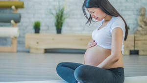 孕婦盤腿坐在瑜伽墊上，在寧靜的工作室中抱著肚子。