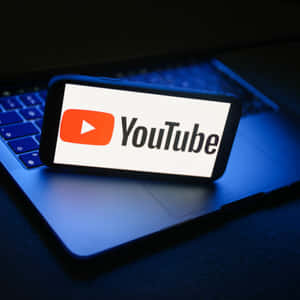 在昏暗的藍光中，智能手機在筆記型電腦鍵盤上顯示YouTube標誌。 — YouTube 壁紙