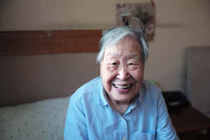 一位老年女性在臥室中身穿藍色襯衫，燦爛地微笑。