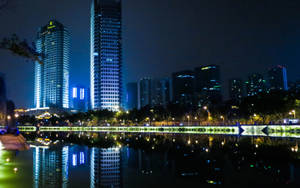 夜晚城市天際線，燈火通明的摩天大樓倒映在寧靜的湖中。