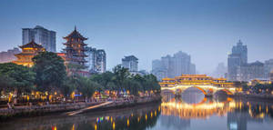 黃昏時分，一座燈光璀璨的傳統橋樑橫跨河流，背景是現代建築。 — 通往泰拉比提亞之橋 壁紙