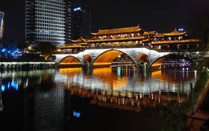 夜晚河流上照明的傳統橋樑，城市燈光倒映在水中。