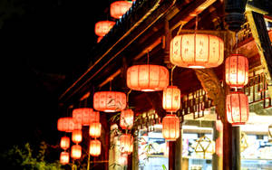 傳統紅色燈籠在夜間照亮木建築，前景有竹子。
