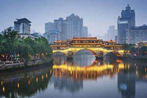 黃昏時分亮燈的歷史中國橋樑，河中有倒影，周圍是城市建築。