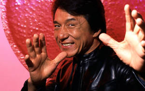 一個穿著黑色皮褸的微笑男人，在粉紅色心形背景下向鏡頭揮手。 — 紅色 壁紙