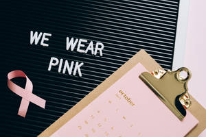 粉紅色絲帶和十月日曆旁邊有一個字母板，上面寫著 WE WEAR PINK。 — 粉紅 壁紙