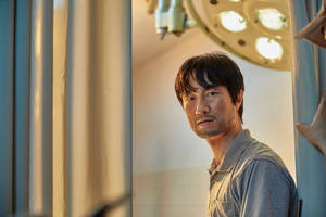 穿著手術袍的男子在明亮燈光下透過醫院窗簾窺視。