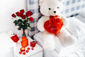 白色泰迪熊拿著紅色心形，上面有 I love you 文字，旁邊有紅玫瑰和情人節裝飾在床上。