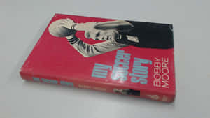 Bobby Moore的復古紅色足球自傳書，封面有球員照片。 — 紅色 壁紙