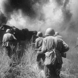 戴頭盔的士兵穿過草地，向煙霧瀰漫的戰場前進。 — 戰爭 壁紙