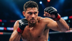一名男性MMA拳手戴著紅色和黑色手套，在明亮的八角籠內出拳。