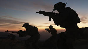 剪影士兵在日落時分持武器越過山丘。