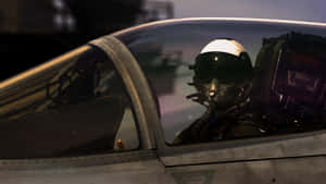穿著飛行服和頭盔的飛行員在黃昏時身處戰鬥機駕駛艙內。