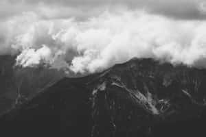 單色山脈，雲朵在其鋸齒狀山峰周圍旋轉。 — MacBook 壁紙