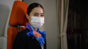 空中服務員戴著口罩和圍巾坐在飛機艙內。