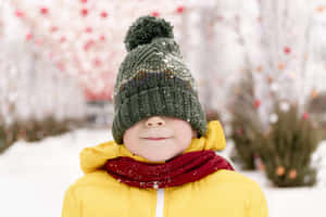 戴著綠色帽子和黃色外套的小孩在雪白的冬日環境中微笑。