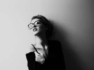 戴眼鏡的女性靠著牆壁的黑白照片。