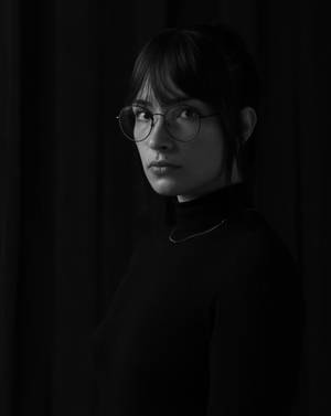 一位戴眼鏡和高領毛衣的女性在昏暗的攝影棚中直視鏡頭。