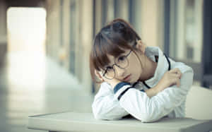 一位戴眼鏡的年輕女子在室內的桌子上將頭靠在手臂上休息。