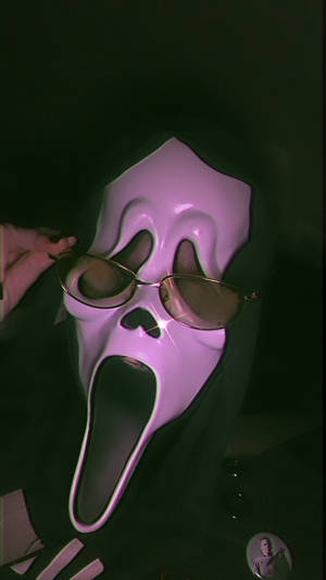 一個粉紅色 Ghostface 面具，配金色框太陽眼鏡，喺黑暗嘅綠色燈光下。 — 尖叫 壁紙