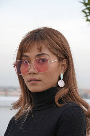 戴著粉紅色太陽眼鏡、身穿黑色高領毛衣和粉彩耳環的女性。