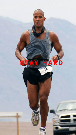 一位男性跑者在比賽中，胸前印有「STAY HARD」字樣，背景為山區地形。