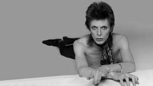 David Bowie 的黑白工作室肖像，赤裸上身躺著，眼神強烈。