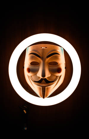 一個白色嘅 Guy Fawkes 面具，被明亮嘅環形燈照亮，掛喺深色木牆上。 — 鬼滅之刃面具 壁紙