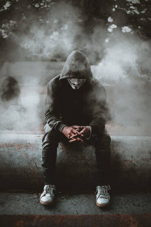 穿著連帽衫和面具的匿名人物坐在混凝土上，被煙霧包圍 — 黑白 壁紙