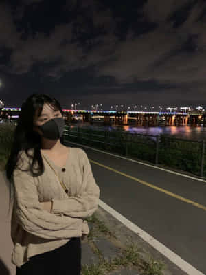 晚上，戴著口罩的人站在燈光璀璨的橋下的河邊。