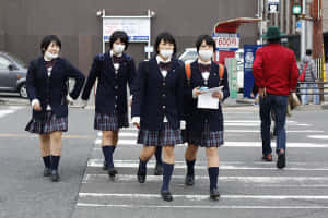 四名身穿校服的女學生佩戴口罩橫過城市街道。