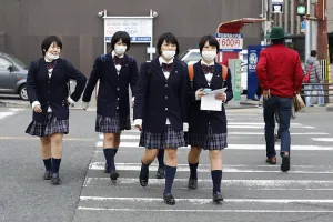 四名身穿校服的女學生佩戴口罩橫過城市街道。