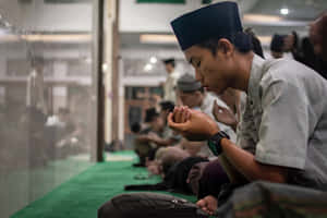 年輕男子在清真寺內雙手合十在綠色地毯上祈禱
