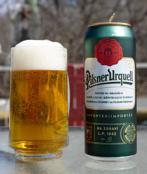 戶外金屬桌上的一杯啤酒和一個 Pilsner Urquell 罐。