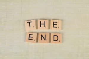 木製 Scrabble 字母牌在米色紋理背景上拼出 the end。