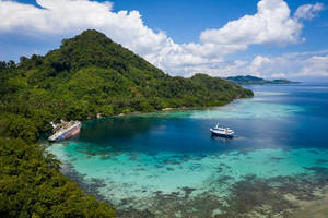 沉沒的遊輪在熱帶島嶼海岸旁，有碧綠的海水和附近的小船。