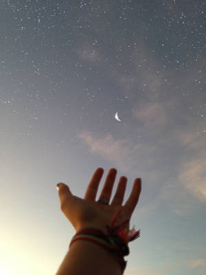 一個人的手伸向夜空中的星星和月亮。