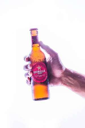 手拿著一瓶帶有冷凝水滴的冰凍Estrella Damm啤酒。