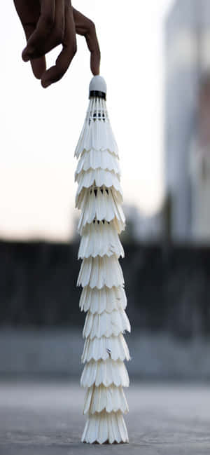 手在黃昏時分於戶外平衡著一疊高高的白色羽毛球。 — iPhone Air 壁紙