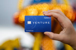 手拎住一張藍色Capital One Venture信用卡，後面有模糊嘅燈光。
