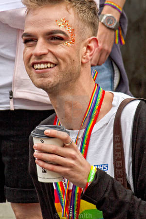 戴著彩虹掛繩和閃粉的男人在Pride遊行中拿著咖啡微笑。