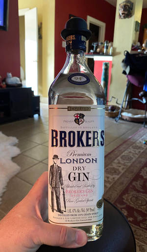 在舒適的客廳中，手拿著一瓶Brokers London Dry Gin。