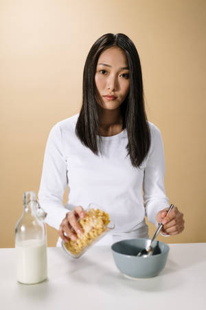 女性將穀物片倒入牛奶杯旁邊的碗中。 — 亞洲 壁紙