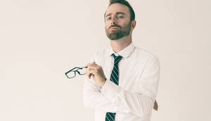 一個穿著商務服裝的男人，手持眼鏡，神情若有所思。