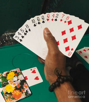 一隻手在綠色遊戲桌上握著扇形攤開的啤牌。