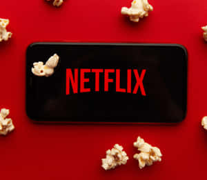 智能手機顯示Netflix標誌，爆谷散落在紅色背景上。