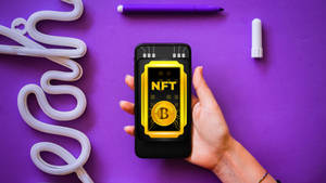 手拿著電話在紫色背景上顯示NFT代幣，帶有霓虹管。