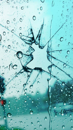 雨滴落在破裂的汽車擋風玻璃上，顯示模糊的藍色背景。